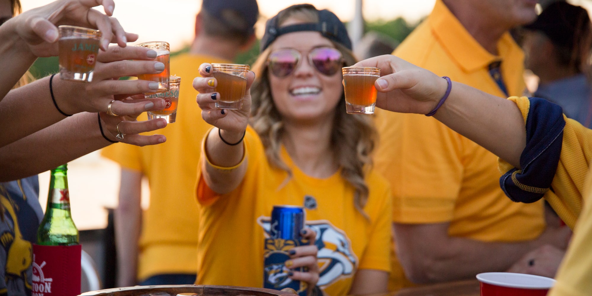 Group of people on the Game Day Water Taxi heading to a Nashville sports game, featuring a woman in sports gear about to toast with friends. The boat offers alcohol for guests.